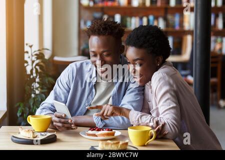 Romantische Zeiten. Schöne afroamerikanische Paar mit Smartphone auf Datum im Café Stockfoto