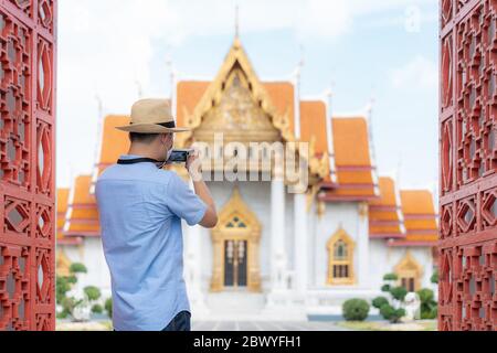 Asian Mann glücklich Touristen reisen mit Maske zum Schutz vor Covid-19 in seinen Ferien und er machte ein Foto mit der Kamera in Temple in Bangkok, Thailan Stockfoto