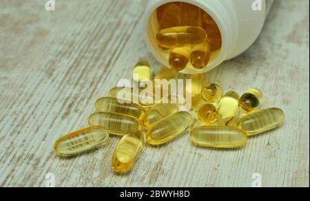 Fischöl Kapseln mit Omega 3 und Vitamin D in einer Plastikflasche auf eine glänzende Textur mit Sonnenstrahlen, gesunde Ernährung Konzept Stockfoto
