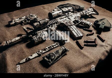 Foto eines getarnten Militärgewehr AR-15 mit Zielfernrohr mit Messer, Pistole und taktischen Handschuhen Seitenansicht. Stockfoto