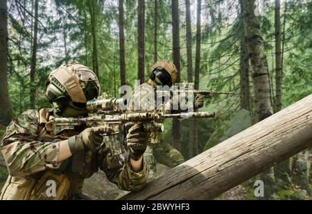 Foto von einem voll ausgestatteten Soldaten in Tarnung sitzen und im Wald zielen. Stockfoto