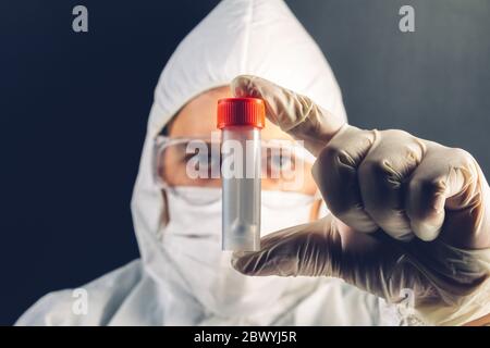 Foto eines Mediziner in Maske, Handschuhe und Schutzanzug mit einem Reagenzglas. Stockfoto