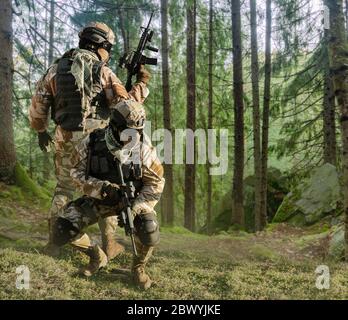 Foto von einem voll ausgestatteten Soldaten in Outfit, Rüstung, Helm, Brille mit automatischem Gewehr posiert auf Wald Hintergrund. Stockfoto