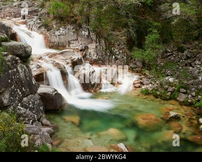 Wasserfall von Mata de Albergaria in der Mitte des Waldes fließt das Wasser die Felsen hinunter bis zum grünen See Stockfoto