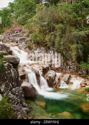 Wasserfall von Mata de Albergaria in der Mitte des Waldes fließt das Wasser die Felsen hinunter bis zum grünen See Stockfoto