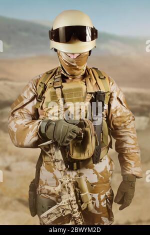 Foto eines voll ausgestatteten Soldaten in Uniform, Rüstung, Helm und Brille in der Wüste stehend und Weste halten. Stockfoto