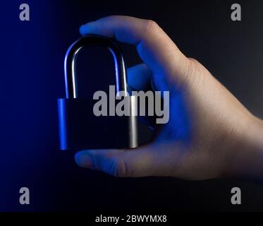 Foto einer blau aufgehellten Hand mit geschlossenem Schloss auf schwarzem Hintergrund, Nahaufnahme. Stockfoto