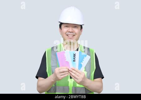 Ein Ingenieur mittleren Alters aus Asien, der ein Bankpassbuch auf grauem Hintergrund in der Hand hält. Stockfoto