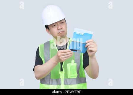 Ein Ingenieur mittleren Alters aus Asien, der ein Bankpassbuch auf grauem Hintergrund in der Hand hält. Stockfoto