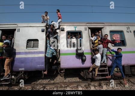 Pendler hängen zwischen den Schienenfahrzeugen und sitzen auf dem Dach eines überfüllten indischen Eisenbahnzuges, Noli Railway Station in der Nähe von Ghaziabad, Delhi, Indien. Stockfoto