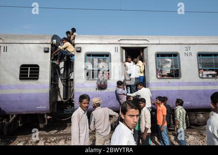 Pendler hängen zwischen den Schienenfahrzeugen und sitzen auf dem Dach eines überfüllten indischen Eisenbahnzuges, am Noli Bahnhof in der Nähe von Ghaziabad, Neu Delhi, in Stockfoto