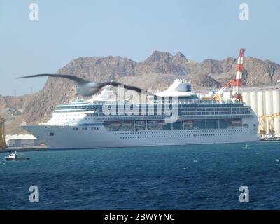 Ein Schiff legt am Hafen an. Muscat, Omans Hafenhauptstadt, liegt am Golf von Oman, umgeben von Bergen und Wüste. Oman, offiziell das Sultanat Oman, ist ein Land an der südöstlichen Küste der Arabischen Halbinsel in Westasien. Die Geschichte reicht bis in die Antike zurück und verbindet Hochhäuser und gehobene Einkaufszentren mit Wahrzeichen auf den Klippen wie den portugiesischen Festungen aus dem 16. Jahrhundert, Al Jalali und Mirani, die sich über dem Hafen von Muscat befinden. Stockfoto