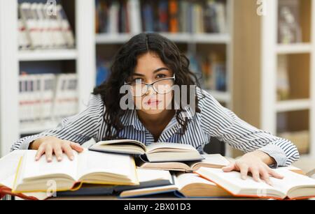 Müde Student lehnt sich an Bücher in der Campus-Bibliothek Stockfoto