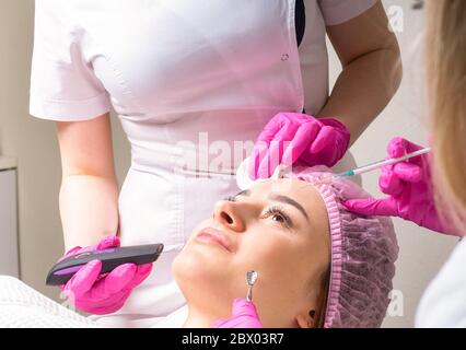 Zwei Kosmetologen arbeiten mit Gesicht eines Patienten zur gleichen Zeit Stockfoto