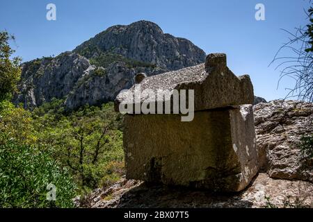 Ein aus Stein geschnitzter Sarkophag liegt an der antiken Stätte Termessos im Taurusgebirge der Türkei prekär am Rande eines Berges. Stockfoto