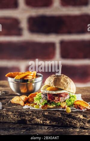 Rinderburger mit Spiegelei, Speck, Salat, Kartoffelkeile und Trauben auf rustikalem Holz Stockfoto