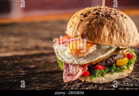 Detail eines Burger mit Rindfleisch, Käse, Ei, Speck, Salat, Paprika in einer rustikalen Umgebung Stockfoto