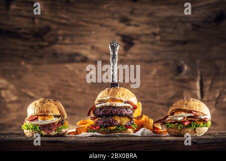 Double Beef Burger, Chicken Burger und ein Beef Burger in rustikaler Holzumgebung mit einem Vintage Messer in den größten Burger gestochen Stockfoto