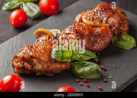 Hähnchenschenkel und Basilikum in einer schwarzen Gusseisenpfanne auf einem Holztisch Stockfoto