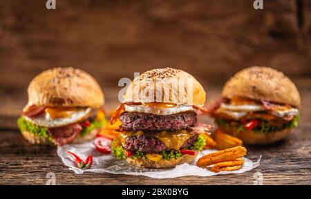 Saftige und leckere Burger-Menü mit Doppel-Rindfleisch-Burger in der Front mit würzigen Kartoffelkeile und Chili und zwei weitere Burger in der Rückseite Stockfoto