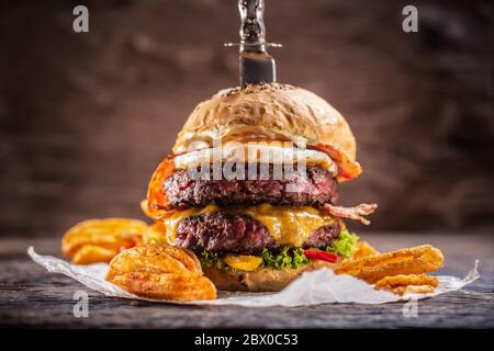 Ein Messerstacheliger Double-Beef Burger mit geschmolzenem Käse, Spiegelei und Speck, Salat und Paprikapoffelkeilen Stockfoto