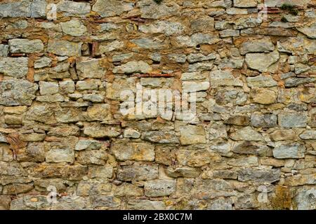 Alte Natursteinmauer mit Pflanzen und Moos, die aus dem Bruchgrund wachsen Stockfoto