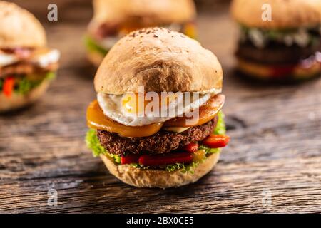 Detail eines Hamburgers mit Cheddar, Spiegelei, Paprika und Salat in einem knusprigen Brötchen, mit drei weiteren Burgern im Rücken Stockfoto