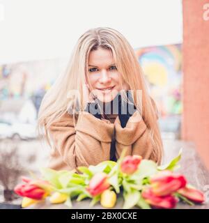 Skandinavische Blondine mit Blumen - niedliche attraktive Mädchen auf der Straße in modischen eleganten Kleidung Stockfoto