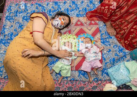 Junge Mutter trägt Maske liegend auf dem Bett mit ihren zwei neugeborenen Zwillingskindern, Aufenthalt Zuhause Einnahme von Extra Care aufgrund Covid-19 Pandemie. Indische Mutter Mit Ihm Stockfoto