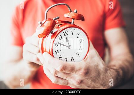 Roter Wecker in den Händen - Einstellung der Zeitschaltuhr auf 10 Minuten vor dem neuen Jahr Stockfoto