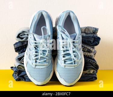 Ein Stapel von verschiedenen Jeans Hosen und blauen Sneakers schließen auf gelb und weiß Hintergrund, lässige Kleidung, Sport-Stil Stockfoto