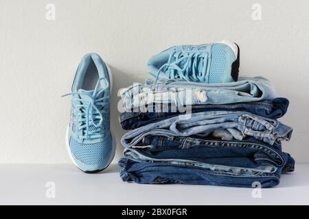 Ein Stapel von verschiedenen Jeans Hosen und blauen Sneakers schließen auf weißem Hintergrund, lässige Kleidung, Sport-Stil Stockfoto