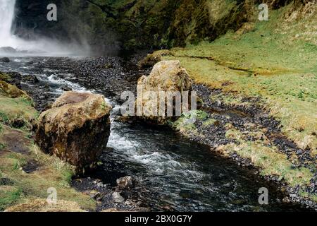 Ein kleiner Gebirgsfluss fließt zwischen zwei Felsbrocken in der mhu, vom Wasserfall Kvernufoss in Island. Stockfoto