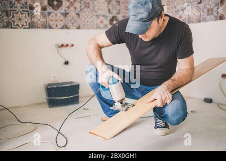 Ein Handwerker schneidet eine Laminatplatte mit einem elektrischen Stichsäge - Bodenbelag Stockfoto