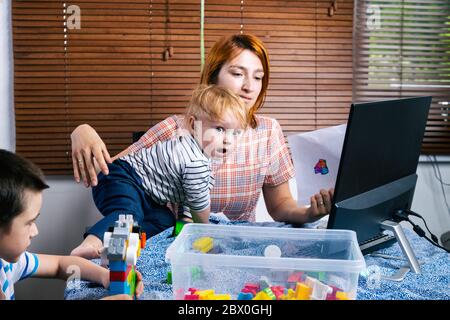 Eine junge Frau Mutter versucht, an einem Computer an einer Remote-Arbeit während der Zeit der Selbstisolierung in Verbindung mit der Coronovirus-Pandemie, weich zu arbeiten Stockfoto