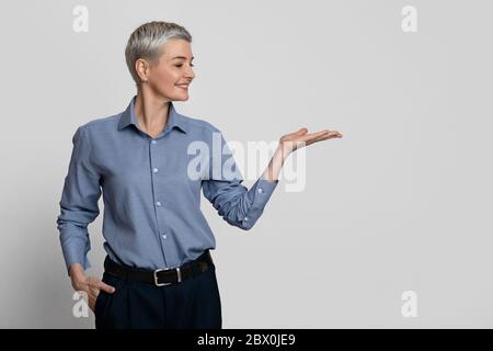 Geschäftsangebot. Lächelnd Reife Geschäftsfrau Demonstriert Etwas An Ihrem Leeren Handfläche Stockfoto