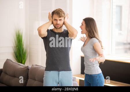 Junger bärtiger Mann schließt die Ohren, während seine Frau schreit Stockfoto