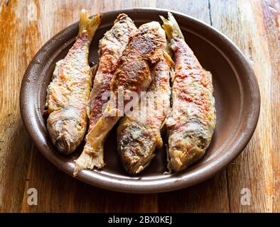 Mehrere gebratene rote Meeräsche auf Keramikplatte auf altem Holztisch in der heimischen Küche Stockfoto