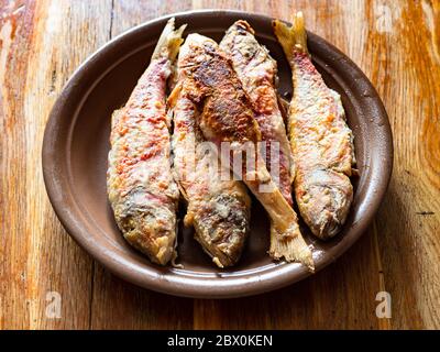 Portion gebratene rote Meeräsche auf Keramikplatte auf altem Holztisch in der heimischen Küche Stockfoto