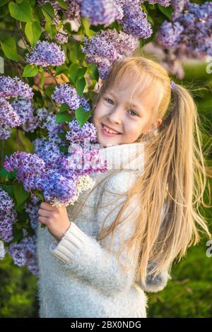 Kleines Mädchen riecht lila Blumen in sonnigen Tag. Stockfoto