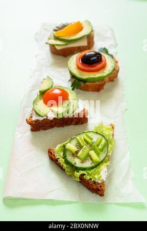 Perspektive Blick auf Reihe von vegetarischen Sandwiches mit Tomaten, Gurken, Avocado, sonnengetrockneten Oliven, Grünes und Käse auf grünem Hintergrund. Wählen Sie Stockfoto