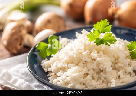 Schüssel mit gedämpftem Reis und Petersilie Tops mit Pilzen und Lecks im Hintergrund Stockfoto