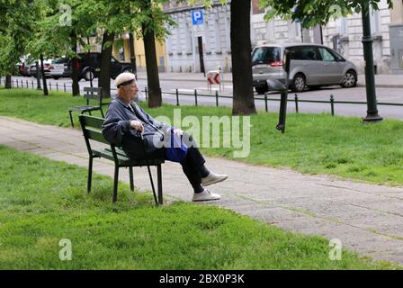 Krakau. Krakau. Polen. Alter Mann mit Gesichtsschutz und Plastikhandschuhen, die auf der Parkbank ruhen. Stockfoto