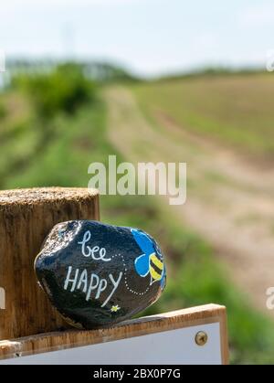 'Bee Happy' gemalter Stein auf Pfosten durch Landweg in Leicestershire während Covid-19 Sperre, England, Großbritannien Stockfoto