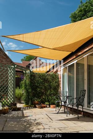 Kleiner Gartenterrasse mit gelben, dreieckigen Sonnenschirmen und blauem Himmel oben an einem sonnigen Sommertag, England, Großbritannien Stockfoto