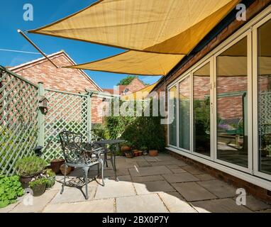 Kleiner Gartenterrasse mit gelben, dreieckigen Sonnenschirmen und blauem Himmel oben an einem sonnigen Sommertag, England, Großbritannien Stockfoto