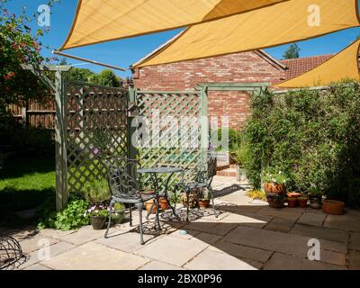 Kleiner Gartenterrasse mit gelben, dreieckigen Sonnenschirmen und blauem Himmel oben an einem sonnigen Sommertag, England, Großbritannien Stockfoto