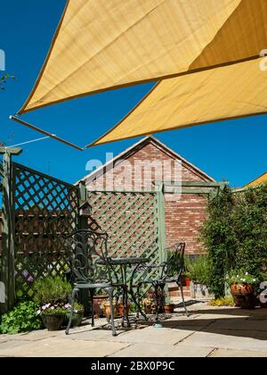 Kleiner Gartenterrasse mit gelben, dreieckigen Sonnenschirmen und blauem Himmel oben an einem sonnigen Sommertag, England, Großbritannien Stockfoto