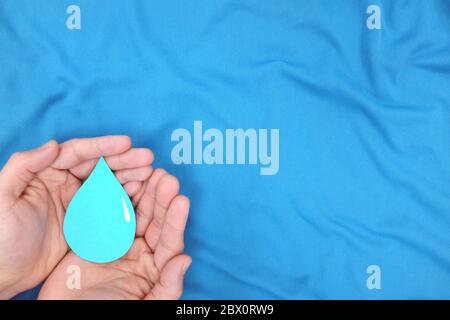 Männliche Hände mit einem blauen Wassertropfen in blauem Hintergrund. Hände waschen, csr, Wasser sparen und Weltmeere Tageskonzept. Draufsicht mit Kopierbereich. Stockfoto