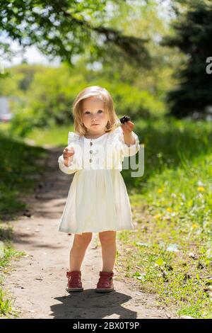 Ein kleines Kind in einem weißen Kleid und blonden Haaren Sammelt Kegel im Wald Stockfoto